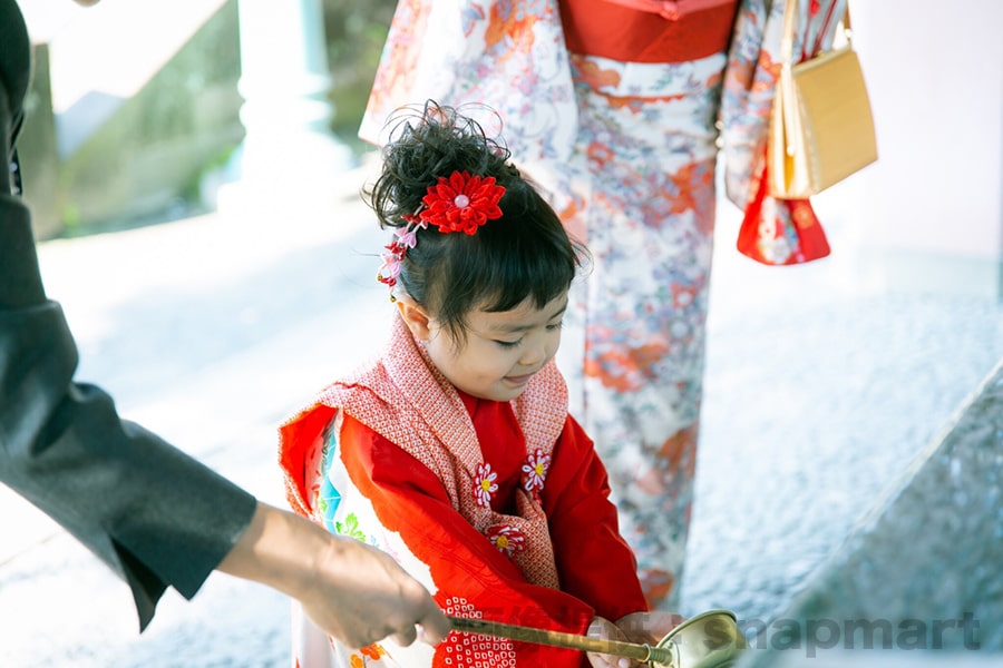 神社本殿前でかわいい表情で記念撮影する七五三三歳ちゃんの様子